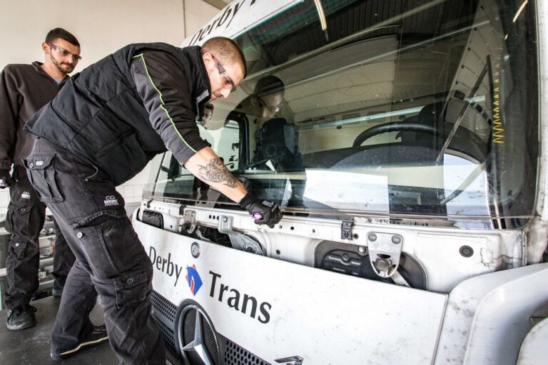 Autóüveg-szerelő a frissen beépített Mercedes teherautó-szélvédő alsó részét és illeszkedését ellenőrzi.