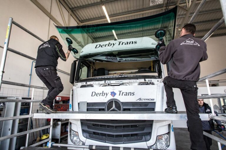 Két Pilis Autóüveg szakember tapadókorongok segítségével emeli a helyére egy Mercedes teherautó új szélvédőjét a műhelyben.